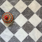 Chequerboard layout featuring Fayrouz White 15.2x15.2cm natural marble tiles with a tumbled finish, paired with black marble tiles, installed diagonally and styled with a decorative patterned dish for added visual contrast.