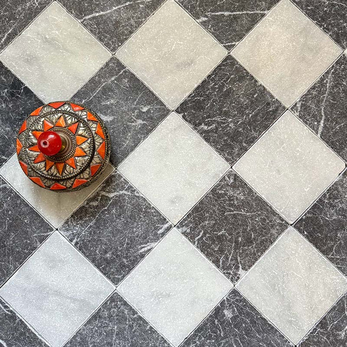 Chequerboard layout featuring Fayrouz White 15.2x15.2cm natural marble tiles with a tumbled finish, paired with black marble tiles, installed diagonally and styled with a decorative patterned dish for added visual contrast.