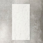 Fayrouz White 30.5x61cm natural marble tiles with a honed finish, featuring soft white tones and subtle grey veining, shown as a single tile sample against a neutral textured backdrop.