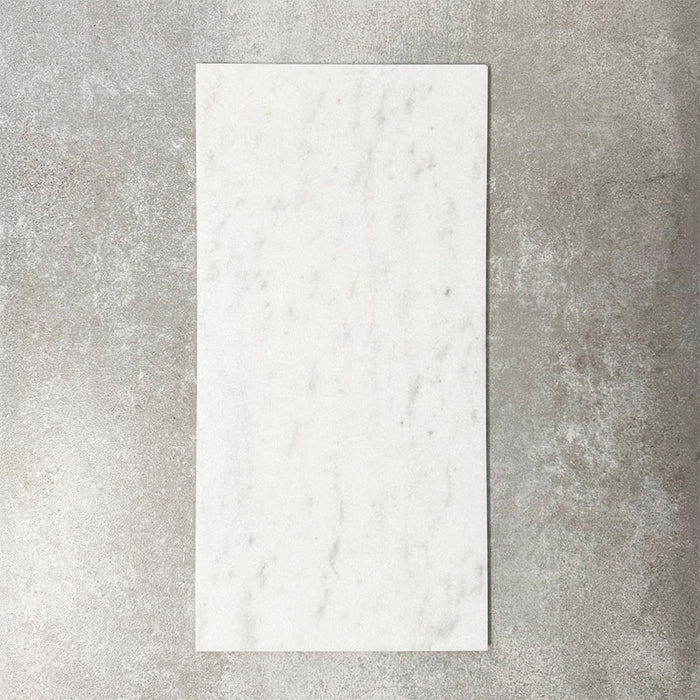 Fayrouz White 30.5x61cm natural marble tiles with a honed finish, featuring soft white tones and subtle grey veining, shown as a single tile sample against a neutral textured backdrop.