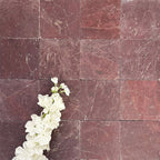 Flat lay of Fayrouz Burgundy Red 15.2x15.2cm natural marble tiles with a tumbled finish, showing rich red tones and natural veining, styled with soft white flowers for contrast and texture.
