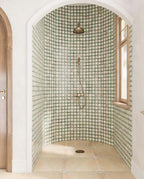 Walk-in shower featuring Zanzibar Moroccan Emerald Green ceramic wall tiles in a repeating Moroccan style star pattern, paired with warm stone effect floor tiles, brushed brass shower fittings, an arched alcove and natural wood window frames for a bright Mediterranean-inspired bathroom.