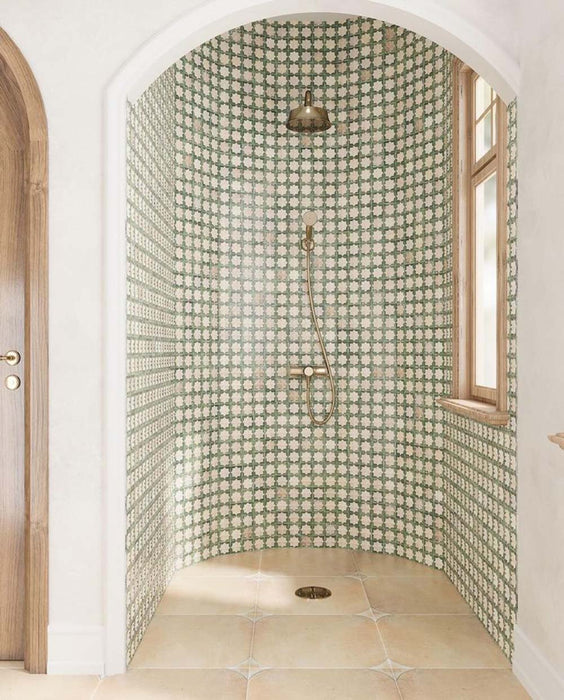 Walk-in shower featuring Zanzibar Moroccan Emerald Green ceramic wall tiles in a repeating Moroccan style star pattern, paired with warm stone effect floor tiles, brushed brass shower fittings, an arched alcove and natural wood window frames for a bright Mediterranean-inspired bathroom.