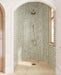 Walk-in shower featuring Zanzibar Moroccan Emerald Green ceramic wall tiles in a repeating Moroccan style star pattern, paired with warm stone effect floor tiles, brushed brass shower fittings, an arched alcove and natural wood window frames for a bright Mediterranean-inspired bathroom.