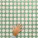 Close-up of Zanzibar Moroccan Emerald Green ceramic wall tiles in a repeating Moroccan style geometric star pattern, shown with a hand for scale to highlight the 31 x 56cm format, subtle tonal variation and textured glazed finish.