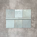 Flat lay of Zellige Aqua Moroccan-style ceramic tiles, showing 13.2×13.2cm square tiles paired with a 3×20cm bullnose trim, highlighting the rounded edge detail, glossy blue-green glaze and natural tonal variation on a neutral background.