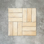 Flat lay of Zellige Arena Marfil Brick 6.5 × 20cm Moroccan-style ceramic tiles, shown in a warm beige and cream colour palette with subtle tonal variation and gently uneven edges, arranged in a basketweave layout on a textured grey background to highlight the handcrafted, zellige-effect finish.