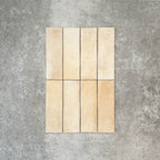 Flat lay of Zellige Arena Marfil Brick 6.5 × 20cm Moroccan-style ceramic tiles, shown in a warm beige and cream colour palette with subtle tonal variation and gently uneven edges, arranged in a vertical brick layout on a textured grey background to highlight the handcrafted, zellige-effect finish.