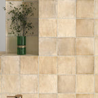 Bathroom wall featuring Zellige Arena Marfil Square 10 × 10cm Moroccan-style ceramic tiles in soft beige and sand tones, installed in a classic grid layout around a freestanding basin and brass tap, with subtle tonal variation and gently uneven edges creating an authentic handcrafted zellige-effect finish.