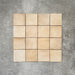 Flat lay of Zellige Arena Marfil Square 10 × 10cm Moroccan-style ceramic tiles in warm beige and sand hues, displaying subtle shade variation and softly uneven edges, arranged in a simple grid on a textured grey background to showcase the handcrafted zellige-effect surface.