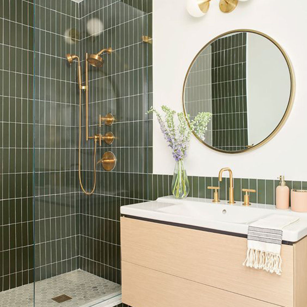 Bathroom shower area featuring Zellige Botanical Green Brick 6.5 × 20cm Moroccan-style ceramic wall tiles in deep botanical green tones, laid in a vertical brick layout, paired with vintage-style brass shower fittings and natural wood accents for a rich, atmospheric zellige-effect finish.