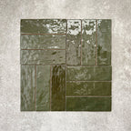 Flat lay of Zellige Botanical Green Brick 6.5 × 20cm Moroccan-style ceramic tiles in deep botanical green tones, arranged in a basketweave layout on a textured grey background, showcasing the glossy glaze, natural tonal variation and handcrafted zellige-effect finish.