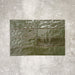 Flat lay of Zellige Botanical Green Brick 6.5 × 20cm Moroccan-style ceramic tiles in deep botanical green tones, arranged in a horizontal brick layout on a textured grey background, showcasing the glossy glaze, natural tonal variation and handcrafted zellige-effect finish.