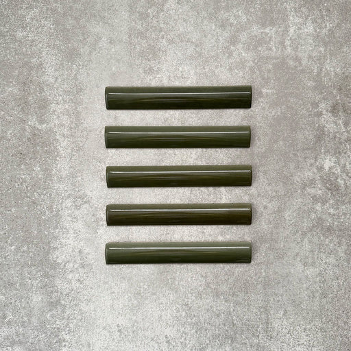 Flat lay of Zellige Botanical Green Bullnose 3 × 20cm Moroccan-style ceramic trim tiles in deep botanical green tones, displayed with a smooth rounded edge and glossy glaze, arranged on a textured grey background to highlight the handcrafted zellige-effect finish and decorative edging profile.