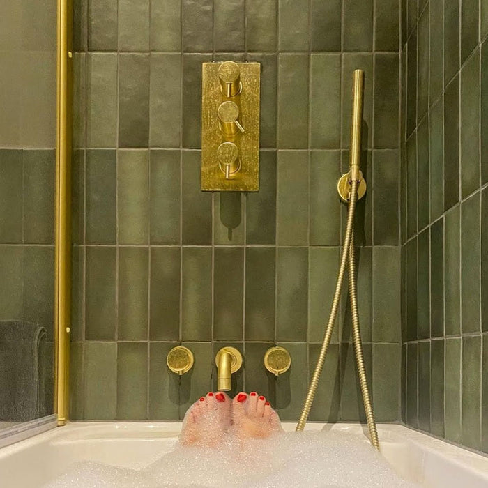 Bathroom featuring Zellige Malachite Green 6.5×20cm Moroccan-style ceramic brick tiles, installed on the walls around a bath and shower, paired with brushed brass fittings, a wooden vanity unit and a stone basin for a warm, spa-like finish.