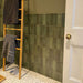 Bathroom featuring Zellige Malachite Green 6.5×20cm Moroccan-style ceramic brick tiles, installed on the walls around a bath and shower, paired with brushed brass fittings, a wooden vanity unit and a stone basin for a warm, spa-like finish.