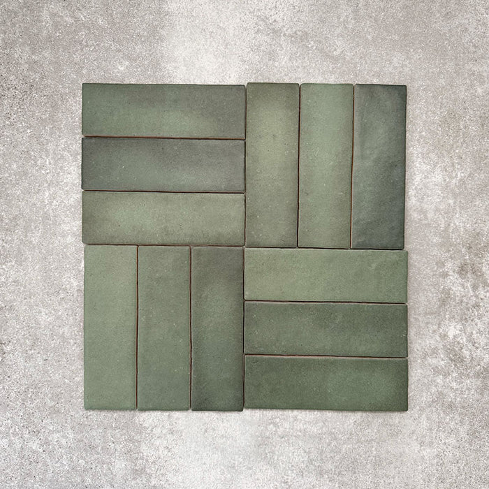 Flat lay of Zellige Malachite Green 6.5×20cm Moroccan-style ceramic brick tiles, arranged in a basketweave layout, showcasing subtle tonal variation, handmade-look texture and rich green glaze on a neutral background.