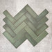 Flat lay of Zellige Malachite Green 6.5×20cm Moroccan-style ceramic brick tiles, arranged in a herringbone layout, showcasing subtle tonal variation, handmade-look texture and rich green glaze on a neutral background.