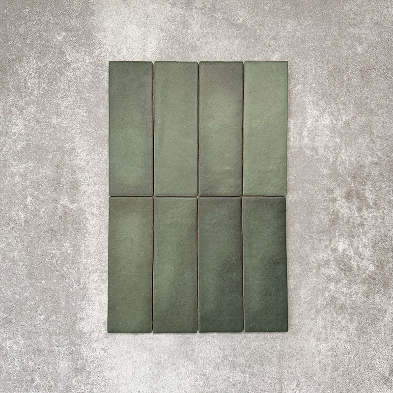 Flat lay of Zellige Malachite Green 6.5×20cm Moroccan-style ceramic brick tiles, showcasing subtle tonal variation, handmade-look texture and rich green glaze on a neutral background.
