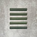 Flat lay of Zellige Malachite Green 3×20cm Moroccan-style ceramic bullnose tiles, showcasing the rounded edge profile, rich green glaze and subtle tonal variation on a neutral background.