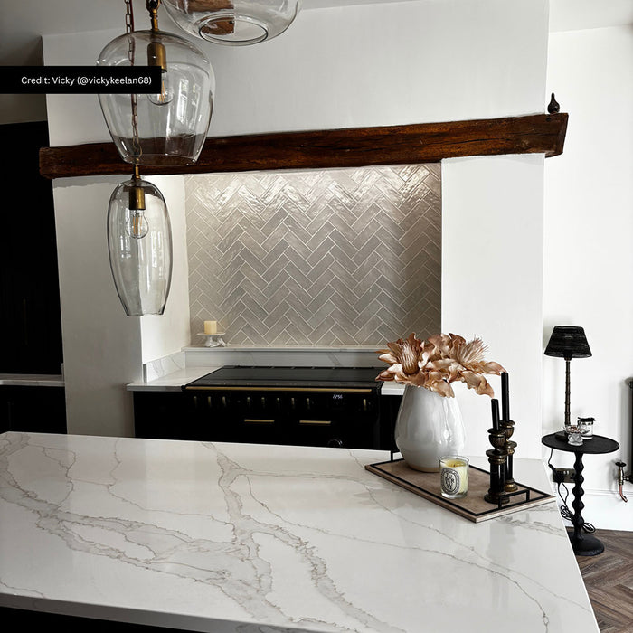 Kitchen featuring Zellige Oyster Brick 6.5x20cm Moroccan-style wall tiles in a herringbone layout, styled with marble worktops, dark wood beams, and black accents for a warm contemporary interior.
