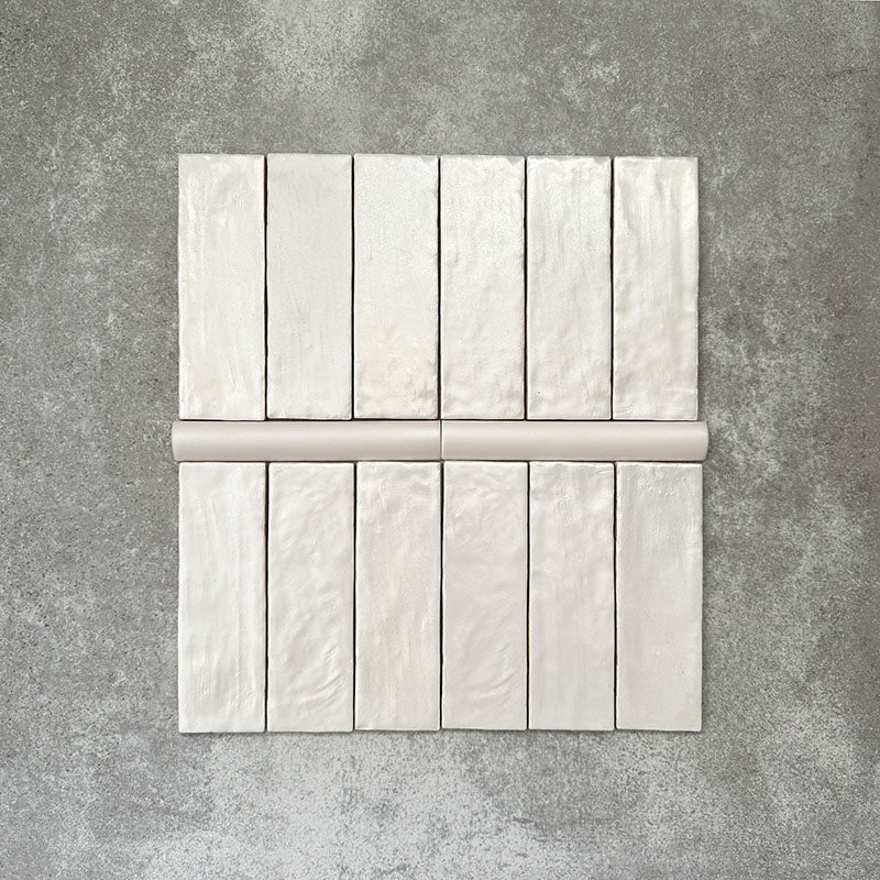 Zellige Oyster brick tiles with matching bullnose trim in an oyster white finish, laid flat to show texture and shape.
