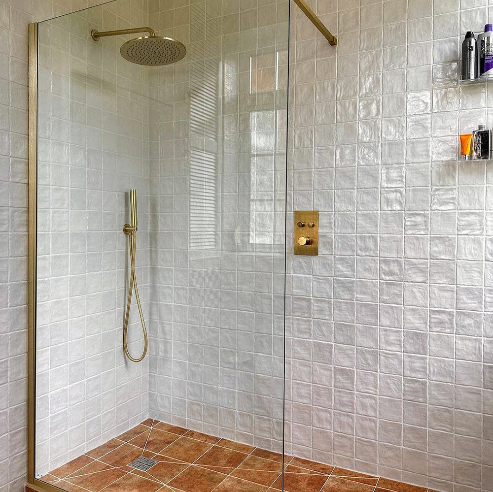 Walk-in shower featuring Zellige Oyster Square Moroccan-style ceramic tiles in a 10 × 10cm format, laid in a uniform grid across the walls, with a glossy oyster-white glaze, gently uneven surfaces and subtle tonal variation, paired with brushed brass shower fittings and a glass screen for a warm, handcrafted bathroom finish.