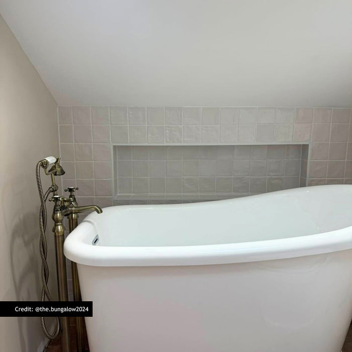 Customer bathroom featuring Zellige Oyster Square Moroccan style porcelain tiles in 10cm x 10cm. Gloss white handmade effect square tiles create a timeless bath surround and recessed shelf, pairing beautifully with a freestanding bath and traditional brass taps.