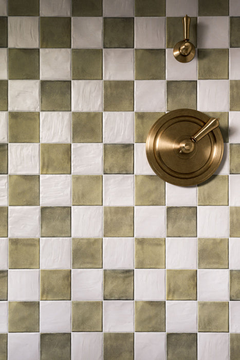Zellige Oyster Square 10cm x 10cm Moroccan style tiles, showcasing their softly irregular surface and subtle tonal variation in a chequerboard layout, paired with aged brass shower fittings for a warm, characterful finish.