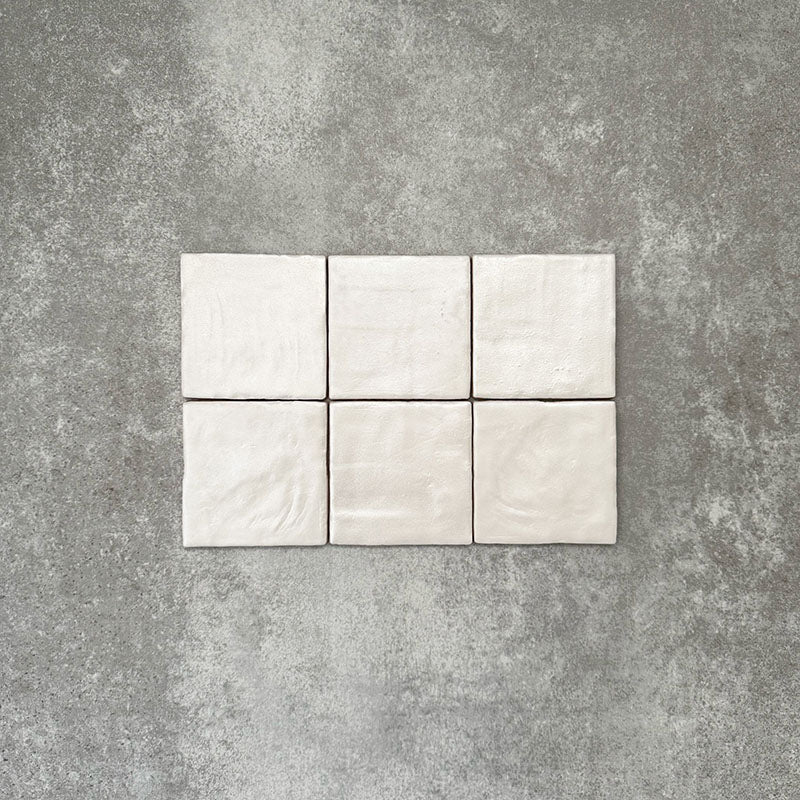 Flat lay of Zellige Oyster Square Moroccan-style ceramic tiles in a 10 × 10cm format, showcasing softly uneven edges, subtle surface ripples and gentle tonal variation that highlight the handcrafted character of the glossy oyster glaze.