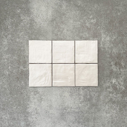 Flat lay of Zellige Oyster Square Moroccan-style ceramic tiles in a 10 × 10cm format, showcasing softly uneven edges, subtle surface ripples and gentle tonal variation that highlight the handcrafted character of the glossy oyster glaze.