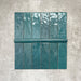 Flat lay of Zellige Peacock Green Moroccan-style ceramic tiles, showing 6.5×20cm brick tiles paired with a 3×20cm bullnose trim, highlighting the rounded edge detail, glossy deep blue-green glaze and natural tonal variation on a neutral background.