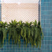 Interior wall featuring Zellige Peacock Green 6.5×20cm Moroccan-style ceramic brick tiles, showcasing rich blue-green tones and a glossy handmade-look finish, styled with trailing plants and a decorative patterned screen for a bold, contemporary feel.