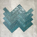 Flat lay of Zellige Peacock Green 6.5×20cm Moroccan-style ceramic brick tiles, shown in a herringbone layout, showcasing deep blue-green tones, a glossy handmade-look glaze and natural tonal variation on a neutral background.
