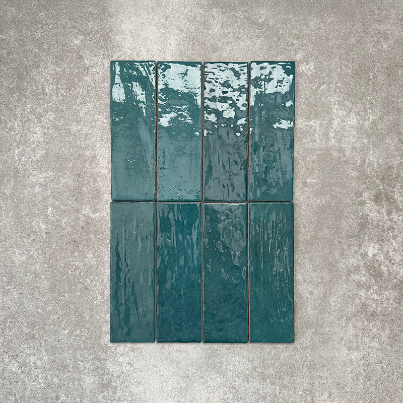 Flat lay of Zellige Peacock Green 6.5×20cm Moroccan-style ceramic brick tiles, showcasing deep blue-green tones, a glossy handmade-look glaze and natural tonal variation on a neutral background.