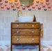 Bathroom vanity splashback featuring Zellige Pink Mist Brick 6.5 × 20cm Moroccan-style ceramic wall tiles in soft pale pink tones, laid in a vertical brick layout behind a white countertop basin with brass tap, paired with a wooden vanity unit, patterned wallpaper and geometric floor tiles to create a warm, playful and handcrafted zellige-effect finish.