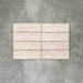 Flat lay of Zellige Pink Mist Brick 6.5 × 20cm Moroccan-style ceramic tiles in soft pale pink and blush tones, arranged in a horizontal brick layout on a textured grey background, showcasing the glossy glaze, gentle tonal variation and handcrafted zellige-effect finish.