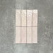 Flat lay of Zellige Pink Mist Brick 6.5 × 20cm Moroccan-style ceramic tiles in soft pale pink and blush tones, arranged in a vertical brick layout on a textured grey background, showcasing the glossy glaze, gentle tonal variation and handcrafted zellige-effect finish.