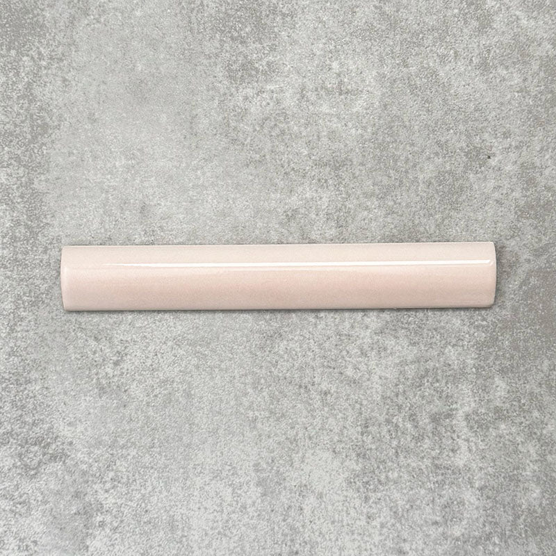 Flat lay of Zellige Pink Mist Bullnose 3 × 20cm Moroccan-style ceramic trim tiles in soft pale pink tones, displayed with a smooth rounded edge and glossy glaze, arranged on a textured grey background to highlight the handcrafted zellige-effect finish and decorative edging profile.