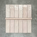 Flat lay showing Zellige Pink Mist Brick 6.5 × 20cm Moroccan-style ceramic tiles paired with a matching Pink Mist Bullnose 3 × 20cm trim tile in soft pale pink tones, arranged on a textured grey background to highlight the glossy glaze, subtle tonal variation and handcrafted zellige-effect finish.