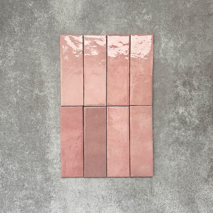 Flat lay of Zellige Rose Pink Brick 6.5 × 20cm Moroccan-style ceramic tiles, shown in soft blush, dusty rose and terracotta pink tones with gentle tonal variation and lightly uneven edges, arranged in a vertical brick layout on a textured grey background to showcase the handcrafted zellige-effect glaze.