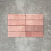 Flat lay of Zellige Rose Pink Brick 6.5 × 20cm Moroccan-style ceramic tiles, shown in soft blush, dusty rose and terracotta pink tones with gentle tonal variation and lightly uneven edges, arranged in a vertical brick layout on a textured grey background to showcase the handcrafted zellige-effect glaze.