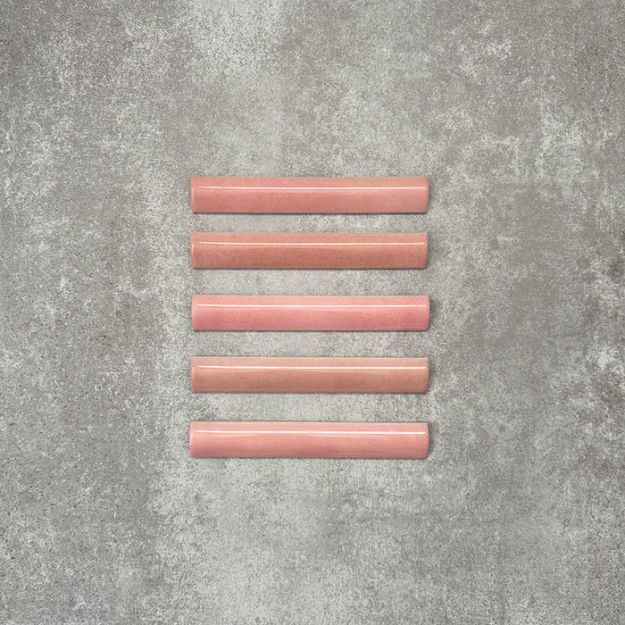Flat lay of Zellige Rose Pink Bullnose 3 × 20cm Moroccan-style ceramic trim tiles in soft blush and dusty pink tones, shown with a smooth rounded edge and subtle glaze variation, arranged on a textured grey background to highlight the handcrafted zellige-effect finish and decorative edging profile.