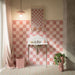Bathroom featuring Zellige Rose Pink Bullnose 3x20cm Moroccan-style tile trim, creating a neat border above pink chequerboard wall tiles, paired with colourful patterned floor tiles and a marble-effect washbasin.