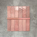 Flat lay showing Zellige Rose Pink Brick 6.5 × 20cm Moroccan-style ceramic tiles paired with a matching Rose Pink Bullnose 3 × 20cm trim tile, displayed in soft blush and dusty pink tones with natural glaze variation and gently uneven edges, arranged on a textured grey background to illustrate the coordinating brick tile and rounded-edge bullnose detail for a handcrafted zellige-effect finish.