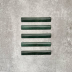 Flat lay of Zellige Royal Green Bullnose 3 × 20cm Moroccan-style ceramic trim tiles in rich deep green tones, displayed with a smooth rounded edge and glossy glaze, arranged on a textured grey background to highlight the handcrafted zellige-effect finish and decorative edging profile.