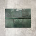 Flat lay showing Zellige Royal Green Square 13.2 × 13.2cm Moroccan-style ceramic tiles paired with a matching Royal Green Bullnose 3 × 20cm trim tile in rich deep green tones, arranged on a textured grey background to highlight the glossy glaze, subtle tonal variation and handcrafted zellige-effect finish.