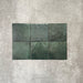 Flat lay of Zellige Royal Green Square 13.2 × 13.2cm Moroccan-style ceramic tiles in rich deep green tones, arranged in a simple grid on a textured grey background, showcasing the glossy glaze, natural tonal variation and handcrafted zellige-effect finish.