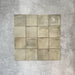 Flat lay of Zellige Weald Green 10×10cm Moroccan-style ceramic square tiles, highlighting soft green and earthy tonal variation, irregular edges and a handmade-look glazed finish on a neutral background.