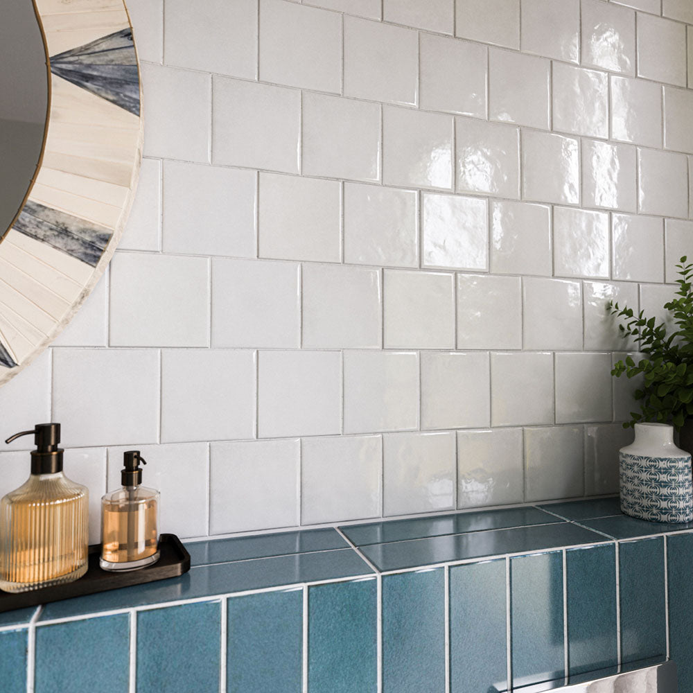 Zellige White Square 13.2cm x 13.2cm Moroccan style tiles, showcasing a softly irregular surface and glossy white finish that catches the light, paired with rich blue tiles and decorative accessories.